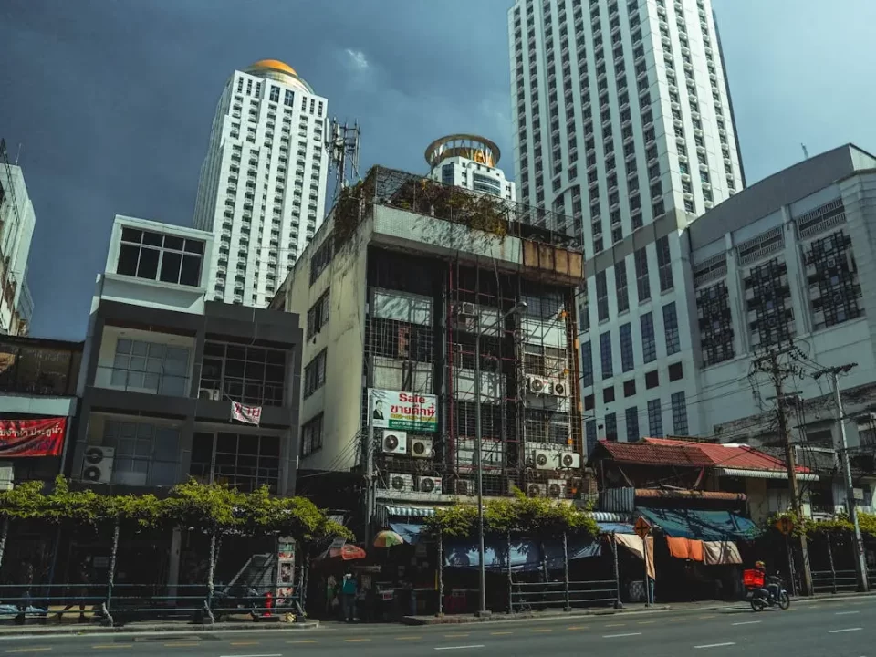 A contrast between an old, gritty shophouse and a modern white skyscraper in bangkok, illustrating the need to upgrade outdated personal asset holdings into robust corporate structures like a labuan company.