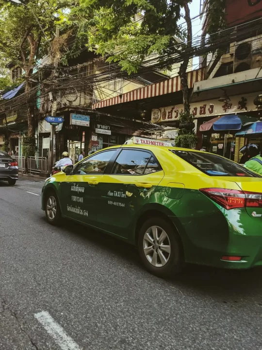 Thailand market insights - serving family businesses and smes in bangkok - cnb trustee, your trusted partner in legacy advisory and will writing services. A green and yellow taxi driving past traditional shophouses in bangkok, thailand, symbolizing the vibrant local economy and the thai-chinese family business sector targeted for estate planning services.